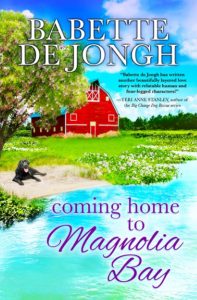 A bright, colorful cover showing a blooming tree and a red barn beside a sparkling blue bay. A black dog lies on the grass by the water. Title reads “Coming Home to Magnolia Bay” by Babette de Jongh.